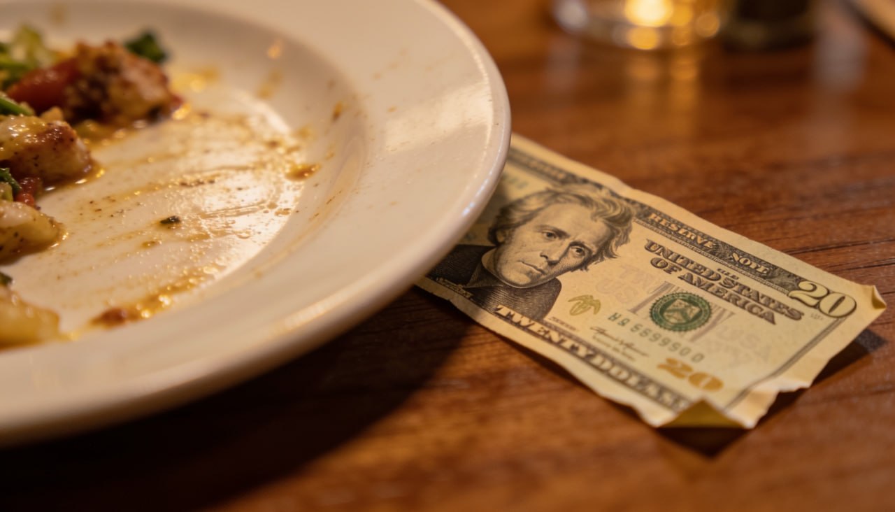 Bahşişin sembolü: boş tabağın yanında 20 dolarlık banknot, ahşap restoran masası üzerinde