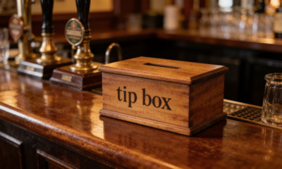 Pub tezgahında ahşap 'tip box' (bahşiş kutusu), arkada bira muslukları ve bardaklar