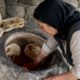 Geleneksel toprak tandır fırınında dikey ekmek pişiren kadın